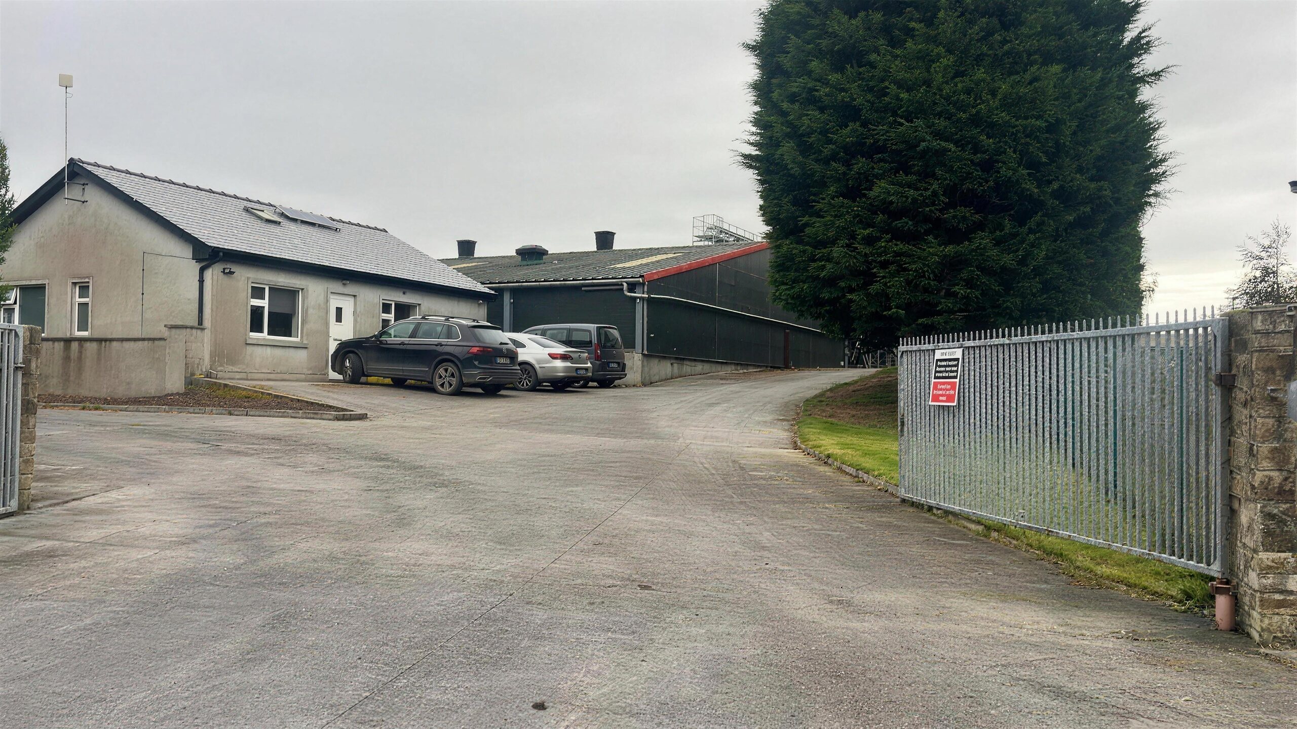 The Kilfilum yard: the asphalt driveway running past the unit buildings to the green-clad warehouse under an overcast Clare sky.